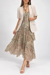 Conjunto compuesto por un vestido largo sin mangas de estampado paisley con volados en capas y un pañuelito a tono, acompañado por una chaqueta beige de manga corta con solapas, botón frontal y bolsillos.