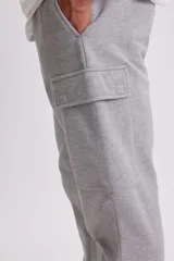 Pantalón deportivo tipo jogger en color gris claro, con diseño cargo que incluye bolsillos laterales. Presenta cintura elástica con cordón ajustable y puños elásticos en los tobillos.