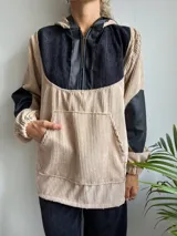 Canguro de pana color beige con capucha, mangas largas de cuero sintético negro y cierre frontal parcial con cremallera.