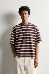 Camiseta de corte relaxed fit con diseño de rayas horizontales en tonos morado, amarillo y blanco. Presenta cuello redondo y mangas cortas.