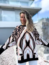 Sweater de punto con diseño oversize y estampado abstracto en tonos negro, beige y blanco. Presenta cuello redondo, mangas largas con puños ajustados y un corte holgado que cae suavemente sobre la figura.