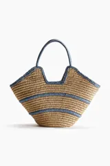 Bolso shopper de doble asa confeccionado en paja de papel trenzada, con diseño estructurado y líneas en tono azul en el cuerpo, asas y bordes.