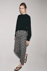 Jeans de tiro medio con corte relajado y largo al tobillo. Presenta un diseño de cinco bolsillos, cierre frontal con cremallera y botón metálico, y un estampado integral de lunares blancos sobre fondo gris oscuro.