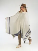 Poncho de hilo color crudo, con diseño de rayas azules y flecos en los bordes. Cuenta con un escudo bordado en la parte posterior.