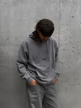 Canguro con capucha gris de corte holgado, con bolsillo frontal tipo canguro y logo pequeño estampado en el centro del pecho.