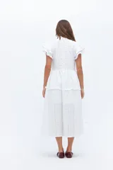 Vestido midi de lino blanco con diseño de broderie, cuello alto, cierre frontal con botones y volados decorativos en los hombros y el cuerpo.