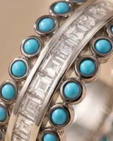 Anillo ancho de plata 925 con hileras de pequeñas piedras turquesas redondas y una línea central de piedras blancas cuadradas facetadas.