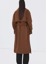 Chaqueta larga tipo trench color marrón, con diseño recto, solapas anchas, doble botonadura, bolsillos laterales y cinturón desmontable de la misma tela.
