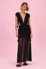 Vestido largo negro de tejido de punto con efecto calado y flecos decorativos. Presenta escote en V profundo, aberturas laterales en la cintura y falda larga semitransparente.