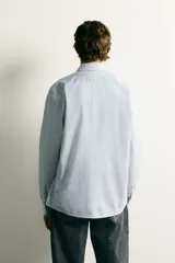 Camisa de corte regular fit confeccionada en tejido de algodón con diseño de rayas verticales finas. Presenta cuello italiano, manga larga con puños abotonados y cierre frontal mediante botonadura.