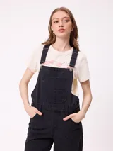 Mono de jean negro de corte recto y holgado, con tirantes ajustables, bolsillos laterales y bolsillo frontal en el pecho.