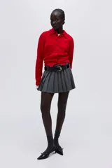 Cárdigan de punto suave color rojo, con cuello redondo ribeteado y cierre frontal de botones oscuros. Presenta puños y bajo acanalados.