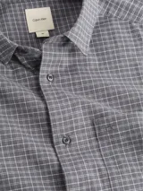 Camisa gris con estampado de cuadros pequeños, de corte regular, cuello en punta, manga larga, bolsillo de parche en el pecho, bajo redondeado y logo bordado en el pecho.