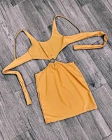 Minivestido color mostaza con escote cut-out, abertura en la cintura unida por un aro metálico y tiras finas.