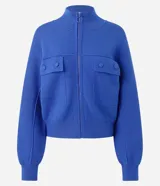 Campera de punto pesado color azul, con cuello alto, cierre frontal con cremallera y bolsillos delanteros con solapa y botones. Cuenta con mangas largas y puños y bajo acanalados.