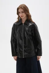 Campera de eco-cuero negro con acabado brillante, cuello camisero, cierre frontal completo y diseño de corte holgado.