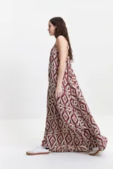 Vestido largo de silueta amplia y fluida, con breteles finos y escote redondeado. Presenta un diseño estampado con motivos geométricos en tonos bordó, beige y gris.