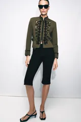 Blazer de estilo militar confeccionado en algodón, con cuello subido y manga larga. Presenta un diseño estructurado con detalle de alamares negros a contraste en el frente, botones metálicos decorativos y trabillas laterales. Cuenta con cierre frontal oculto y forro interior.