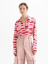 Camisa de seda con estampado de labios en tonos rojos y rosas. Presenta cuello clásico, cierre frontal con botones ocultos y mangas largas con puños abotonados.