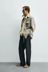 Parka relaxed fit color gris, confeccionada en tejido técnico ligero, con cuello solapa, manga larga con puño abotonado, cuatro bolsillos de plastrón con solapa en el frente, cintura ajustable con cordón y cierre frontal de botones.