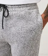 Pantalón de jogging gris jaspeado, con cintura elástica ajustable con cordón, bolsillos laterales y traseros, y puños ajustados.