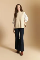 Chaleco de tejido de punto en color crema, con cuello alto y diseño acanalado. Presenta una silueta relajada con aberturas laterales.