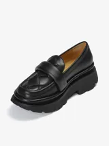 Mocasín negro de plataforma robusta con capellada de cuero trenzado y banda superior acolchada.