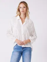 Camisa de gasa ligera y traslúcida, color blanco, con intrincados bordados búlgaros y motivos botánicos distribuidos en toda la prenda. Presenta una guarda bordada que recorre la línea de botones, el ruedo y los puños. Tiene cuello con solapa y abertura central con botones. La silueta es amplia y relajada, con mangas largas y un canesú en la espalda para una caída impecable.