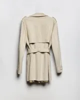 Campera trench de gabardina en color beige, con solapa cruzada, doble botonadura frontal, hombreras y cinturón ajustable para anudar en la cintura. Presenta bolsillos delanteros y puños ajustables con tiras.