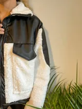 Campera con cierre frontal, de cuero sintético negro y corderito blanco, con cuello solapa y bolsillos plaqué.