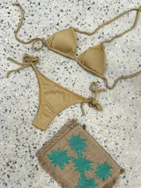 Bikini color dorado brillante, con corpiño triangular de atar al cuello y espalda, con almohadillas desmontables. La bombacha es vedetina con tiras ajustables a los costados.