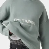 Suéter de punto grueso color verde agua, con corte cuadrado y ligeramente corto. Presenta cuello redondo, puños y ruedo acanalados, y el logo de la marca Eme Studios tejido en jacquard en el frente.