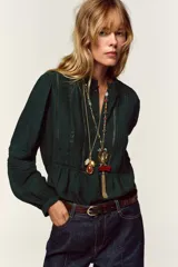 Camisa verde oscuro con cuello de volante y manga larga, detalles de entredoses a tono y cierre frontal con botones forrados.