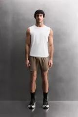 Pantalón corto deportivo color marrón oliva, confeccionado en tejido técnico ligero y elástico, con forro interior. Presenta cintura elástica ajustable con cordón, bolsillos frontales, bolsillo de seguridad trasero con cierre y aberturas laterales en el bajo.