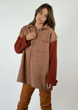 Chaqueta marrón con diseño de espiga, cuello camisero, cierre con botones y un bolsillo de parche en el pecho. Las mangas son largas y de punto color ladrillo.