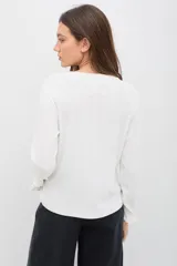 Remera de manga larga color blanco, confeccionada en tejido suave con textura acanalada. Presenta volados verticales decorativos en el frente y en los puños, con un calce cómodo y favorecedor.