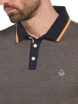 Polo de manga corta con tejido jacquard texturizado en tonos oscuros. Presenta cuello tipo polo en color azul marino con detalles de líneas en naranja y blanco, tapeta con botones y logo de la marca bordado en el pecho.