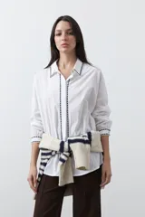 Camisa blanca de manga larga con detalles bordados en contraste a lo largo de la botonadura, el cuello y los puños. Presenta una silueta relajada y un diseño clásico con un toque artesanal.