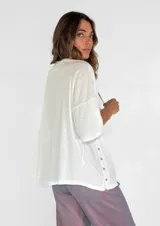 Remera color amarillo con cuello redondo y mangas cortas anchas con detalle de botones en los laterales. Diseño holgado con efecto gastado.