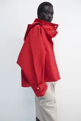 Cazadora roja de cuello subido con capucha y manga larga, bolsillos delanteros y cierre frontal cruzado con botones a presión dorados.