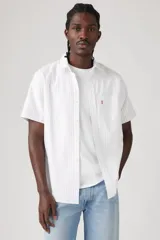 Camisa blanca a rayas verticales finas, de manga corta, con cuello clásico, cierre frontal con botones y un bolsillo en el pecho.