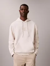Buzo con capucha de Calvin Klein en color beige, confeccionado en mezcla de algodón y poliéster. Cuenta con bolsillo tipo canguro frontal, cordones ajustables y el monograma de la marca bordado en el pecho.
