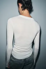 Top de punto fino y semitransparente color gris claro, con cuello redondo y manga larga.