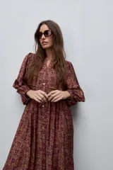 Vestido largo de silueta amplia y caída fluida, con estampado y recortes fruncidos que aportan movimiento. Presenta escote con abertura, cierre frontal con botones y mangas largas de volumen amplio con puños elastizados.