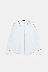 Camisa blanca de popelín con vivos negros a contraste en el cuello, el frente y los puños. Presenta un corte holgado y mangas largas con puños anchos.