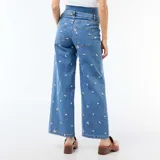 Pantalón de embarazo de corte ancho y tiro alto, confeccionado en denim azul con bordados de pequeñas flores blancas. Presenta un diseño cómodo con cintura elástica adaptada para el periodo de gestación.