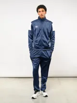 Conjunto deportivo Umbro compuesto por campera de cuello alto con cierre frontal y pantalón de corte recto. La campera presenta bloques de color blanco en los hombros y el logo de la marca bordado en el pecho. Confeccionado en tejido sintético con acabado satinado.