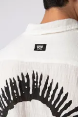 Camisa de manga corta confeccionada en lino, de corte relajado y cuello clásico. Presenta un diseño minimalista en color blanco con textura natural.