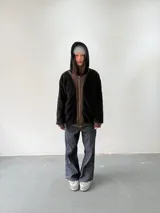 Campera reversible con cierre frontal. Un lado confeccionado en algodón color marrón con estampa plastisol en color naranja, bordados con apliques y capucha. El otro lado confeccionado en tela polar de pelo largo color negro con capucha.