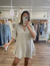 Vestido corto de lino color beige claro, con escote en V y mangas cortas con volados. El ruedo del vestido también presenta un detalle de volado.